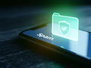 Smartphone toont e-mail inbox met beveiligingsmeldingen, groen schild icoon en doorkruiste spam map op houten bureau